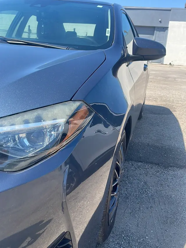 Close-up of a dark blue car’s front fender and headlight with a clean finish